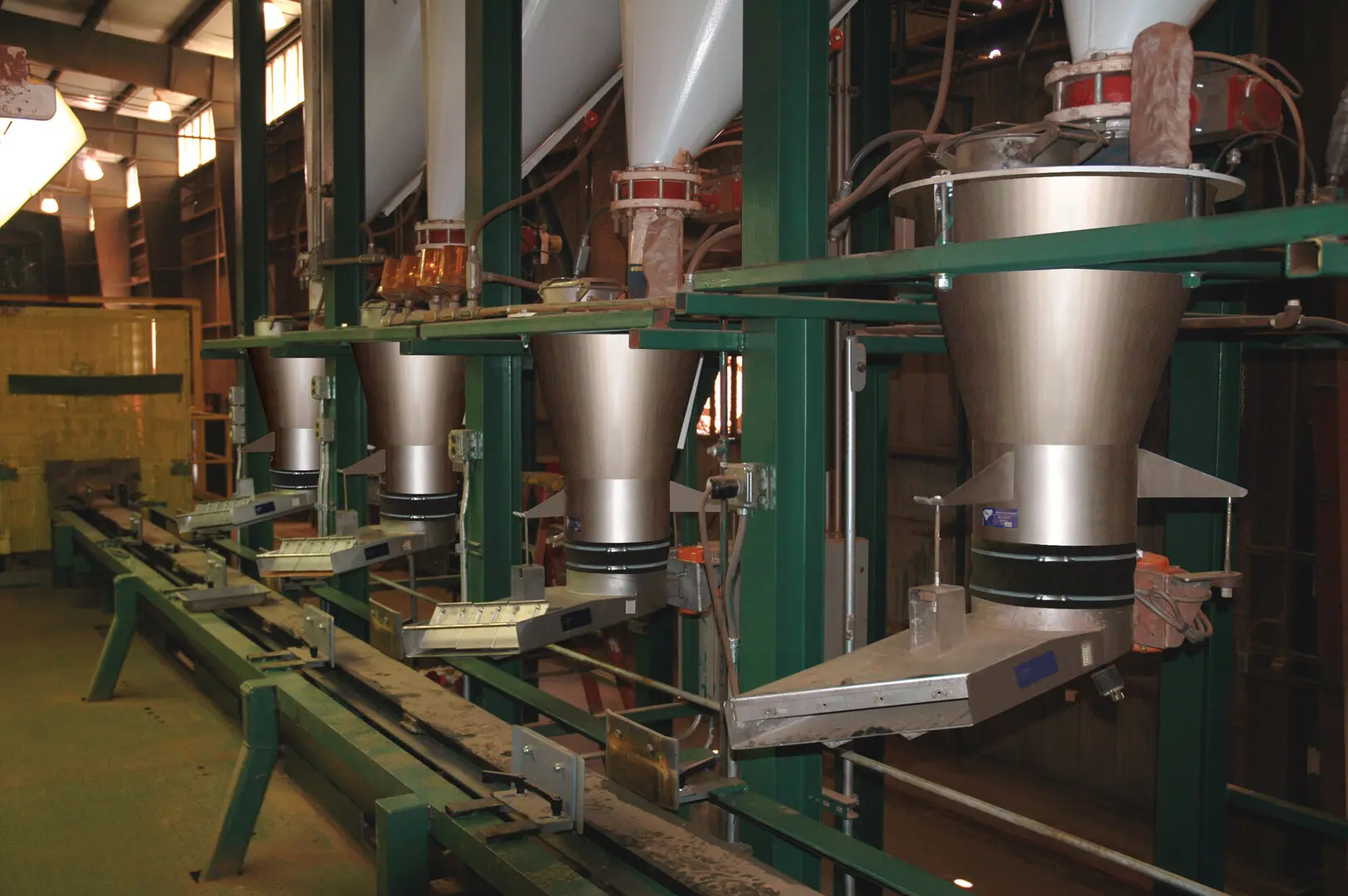 Row of vibratory feeders applying sand mixtures to a manufacturing line